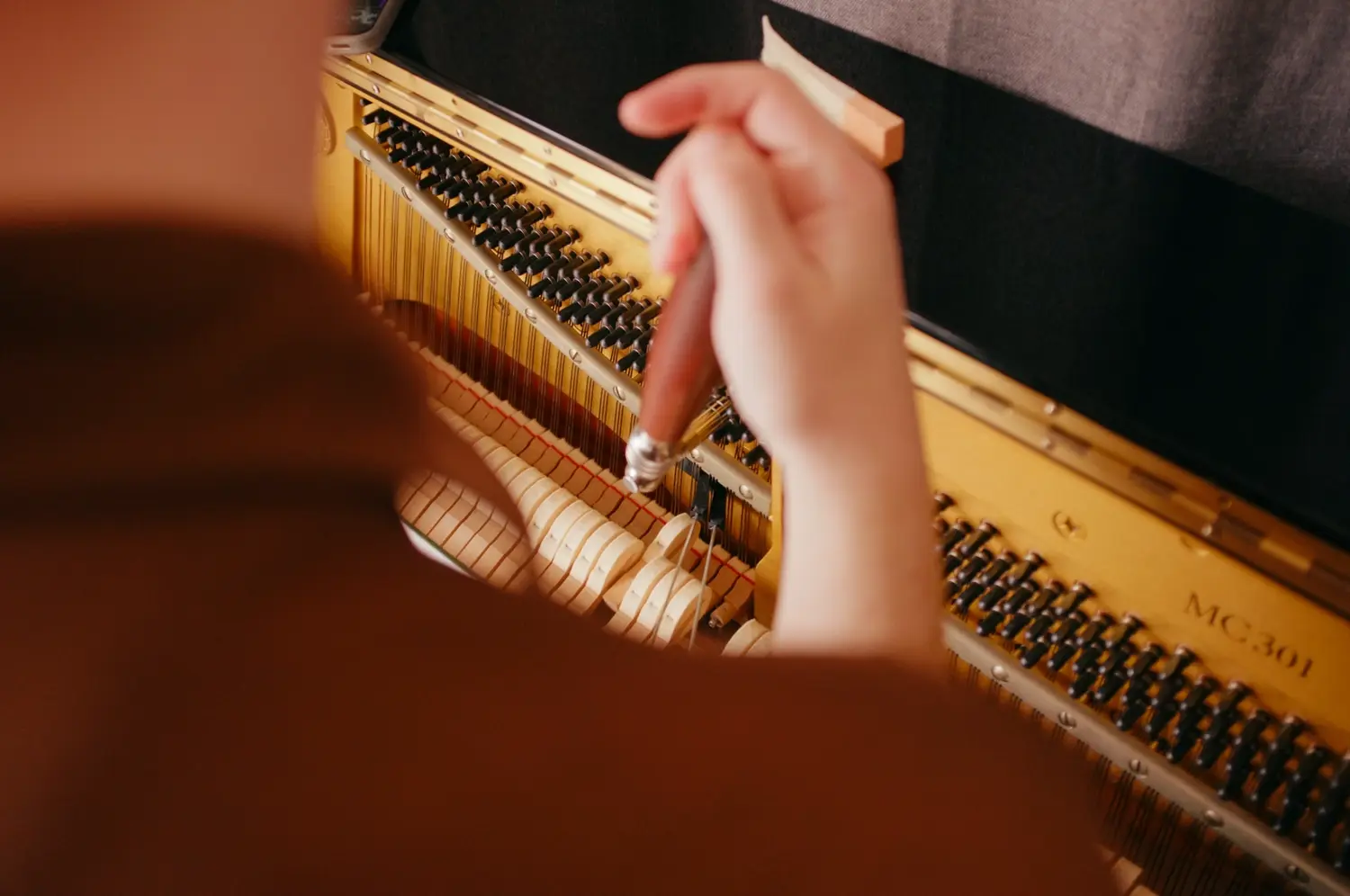 Close view of Reuben using a tuning lever inside an upright piano